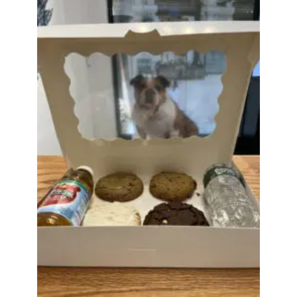 A box of cookies and other treats with a dog in the background.